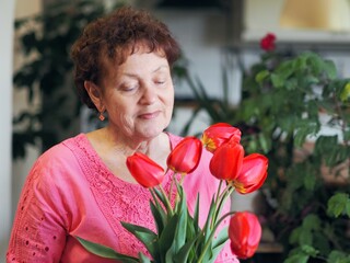 Charming old woman grandmother in bright clothes with a bouquet of tulips at home.