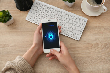 Woman holding smartphone with locked screen at table, top view