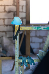 Blue respirator and rubberized black gloves hang on scaffolding, vertical photo
