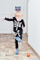 A child in a skeleton costume plays football in the hallway of the house - 503861871