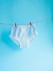 Panties for girls white in blue polka dots hang on a rope attached with a clothespin background on...