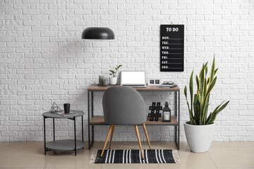 Interior of modern workplace with laptop and board with to do list on white brick wall