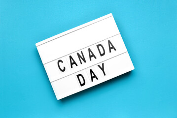 Board with text CANADA DAY on color background