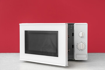 Modern microwave oven with opened door on table against color background - obrazy, fototapety, plakaty