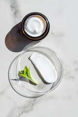 Open cream in a jar and moisturizer smear in petri dish on marble background. Beauty facial cosmetic product texture top view. Body care lotion
