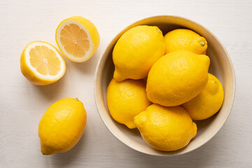 Whole fresh lemons in rustic bowl next to cut lemon from above.