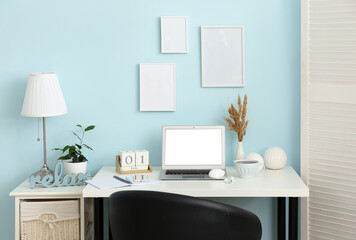Stylish workplace with modern laptop, mobile phone, earphones and decor near color wall in room interior