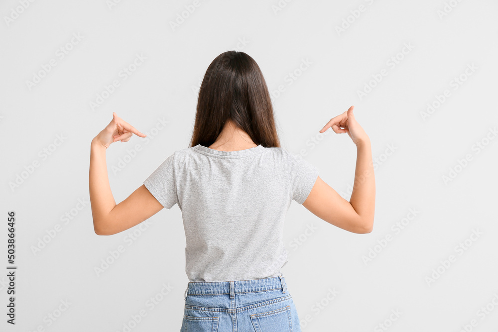 Wall mural Pretty young woman in stylish t-shirt on light background, back view - Wall murals