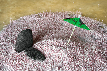 On a pink sand background, a bamboo umbrella and natural stones. Installation of a beach holiday. The concept of travel.