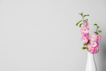 Ceramic vase with blooming branches near light wall, closeup