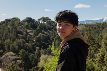 Portrait of teenage Asian boy against forest and sky