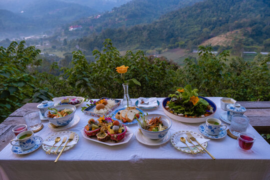 Breakfast Table In The Mountains Of Thailand Chiang Mai, Wooden Served Festive Table With Homemade Food And Drinks, Fresh Fruits And Flowers Under A Pine Tree On A Sunny Day. Luxury Breakfast. 