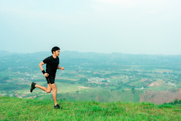 Obraz premium Young Asian runner, wearing black sportswear, running on a big mountain trail, cool morning, windmills, and sky in the background..