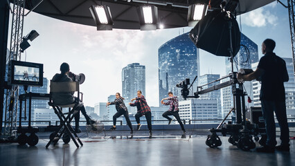 Music Clip Studio Set: Shooting Hip Hop Video Dance Scene with Three Professionals Dancers Performing on Stage with Big Led Screen with Modern City Background. Director and Cameraman in Backstage.