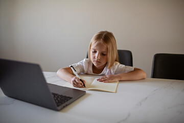 Pretty schoolgirl studying homework during her online lesson at home during quarantine covid-19 