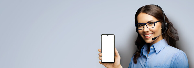Customer support phone operator in glasses and headset holding showing smartphone cellphone mobile with white mock up screen on grey background. Consulting and assistance service call center.