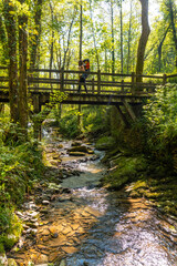 A mother with her son in her backpack crossing a wooden bridge in the Pagoeta park in Aia, Guipuzcoa. Basque Country