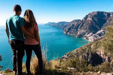 Loving couple with panoramic view from hiking trail Path of Gods near coastal towns Positano, Praiano. Trekking Lattari Mountains, Apennines, Amalfi Coast, Campania, Italy, Europe. Mediterranean Sea