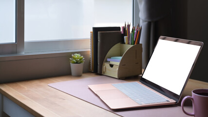 Contemporary workplace with laptop computer, coffee cup and supplies on wooden table.