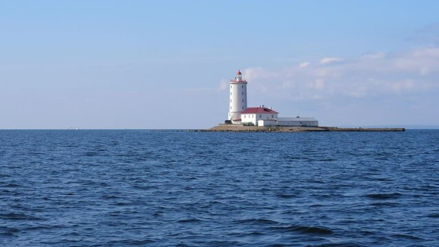 Lighthouse Tolobukhin located on small isle near Kronshtadt island, old fortified navigational light building. Calm waters of Gulf of Finland on fore. Light-keeper house seen near thick white tower