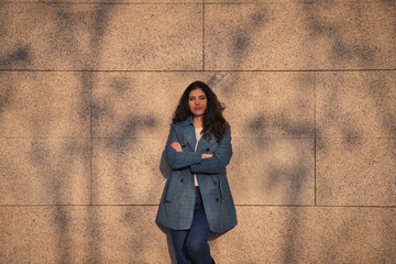 Beautiful young woman with curly brown hair and upturned nose dressed in fashionable clothes poses for photos as a super model on a brown background. Concept of beauty and fashion.