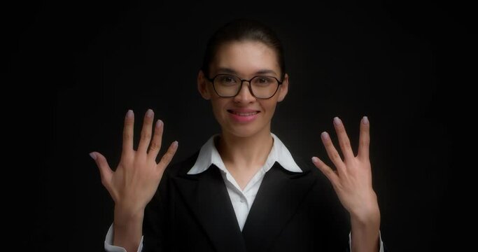 Positive asian woman in glasses and business clothes, smiling, shows nine fingers with her hand. Businesswoman counts with her fingers on her hand. Isolated on a black background.