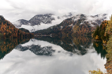 Mountain lake surrounded by autumn mixed forest in fog and snow