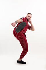 Tattooed man posing in studio on white background. Doing karate, fight, jumping, high leg kick. Red stripe sportswear.