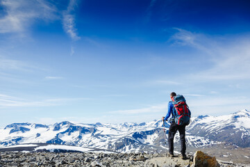 Fototapeta premium Hiker with backpack standing on top of a mountain and enjoying tne view
