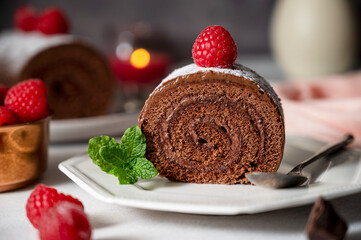 Chocolate roll cake or swiss dessert cake with raspberries. Romantic mood with candles.