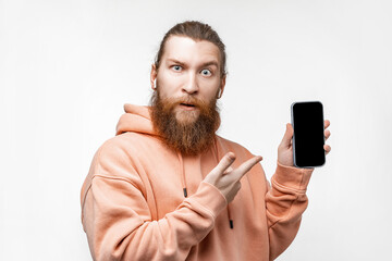 Scandinavian handsome surprised man holding a phone and points to black screen mockup with...