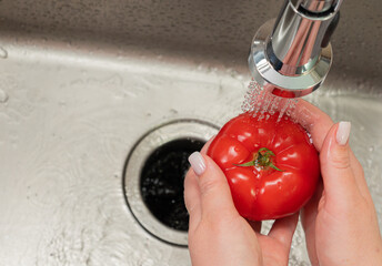 girl's hands washing a tomato in the kitchen