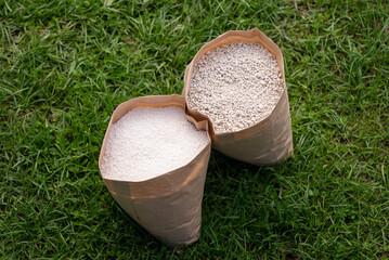 Two bags of fertilizer on grass. NPK and granulated nitrate fertilizers in paper bags