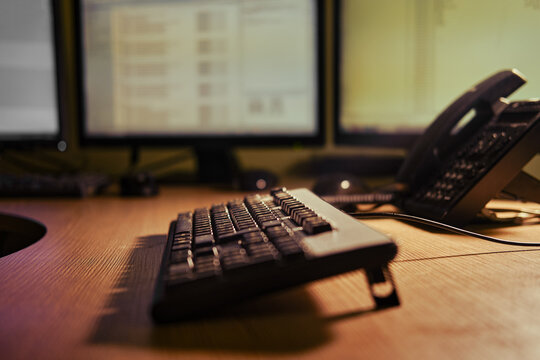 Computer keyboard on an office desk with monitors and a phone, close-up