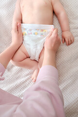 A mother woman puts on a diaper for a baby boy. Mom dresses child in clothes on the bed.