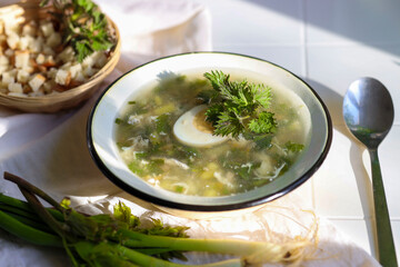 Soup with fresh nettles, egg, meat and potatoes. Fresh nettle leaf on the kitchen table a rustic background.