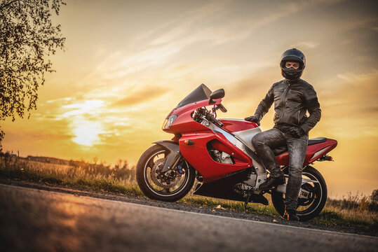 Motor biker is standing on the road on the sunset background.