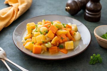 Roasted or baked root vegetables with fresh herbs, orange vegetables on plate. Vegan food.