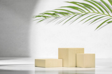 Wooden natural cube podium in white and grey marble interior with shadow. Summer modern showcase with cube wooden podium with green palm leaf in sunlight, shadow on grey marble wall