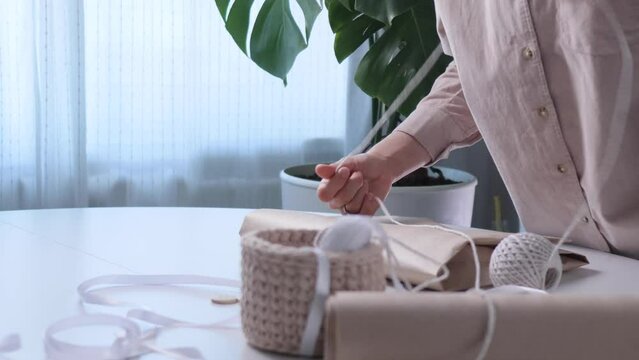 Unrecognizable woman is using craft eco paper for wrapping thing for packaging a gift. Close-up hands 4K video