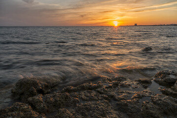 Tramonto sul mare con riflessi del sole sull'acqua, cielo con nuvole e scogli.