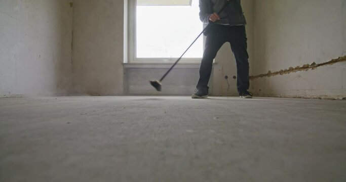 Static wide shot of sweeping the floor in an empty room. A lot of dust in the air. Man walking out of the frame at the end.