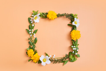 Summer or spring composition on a orangr background. Yellow and white flowers and green leaves with a copy space wreath top view. Summer, spring floral concept