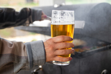 Female hand holding glass of beer while cooking on a barbecue grill.