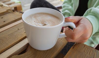 Woman hand holding a cup of coffee on wooden table in garden.