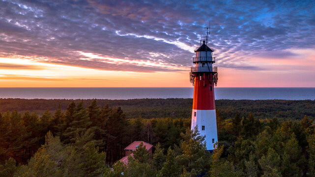 Aerial view of the lighthouse during sunset. Orange sky, dark clouds. Sea in the background.