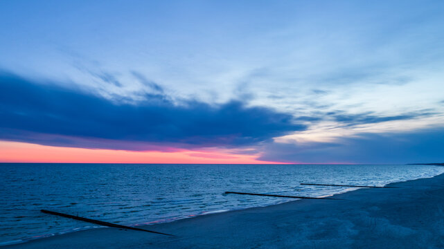 Sea after sunset, orange sky and dark clouds. View of the wooden breakwater. 