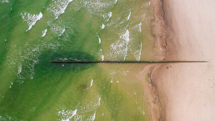 Top down view of the sea and sandy beach in a daylight. View of the breakwater and sea waves.