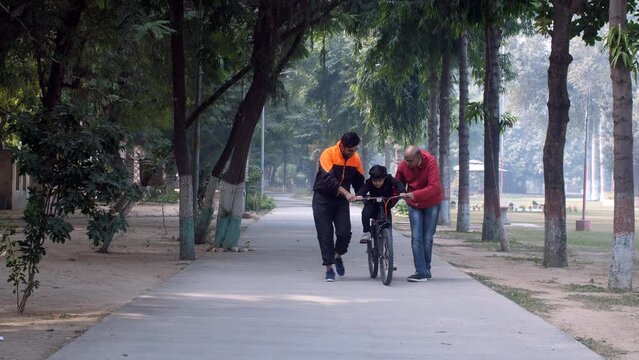 A sweet schoolboy learning to ride a bicycle with his father and grandfather - parental bonding  cycling. A caring father with his son in the park - father-son bonding  modern-day parenting  three ...