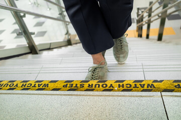 Watch your step sign sticker on the stairs at public area with a person walking up the stairs